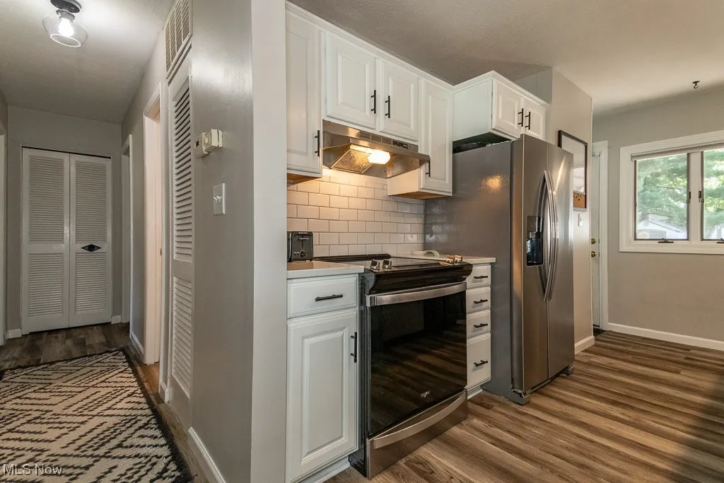 Kitchen featuring stainless steel electric range, under cabinet range hood, tasteful backsplash, dark wood-style floors, and white cabinetry