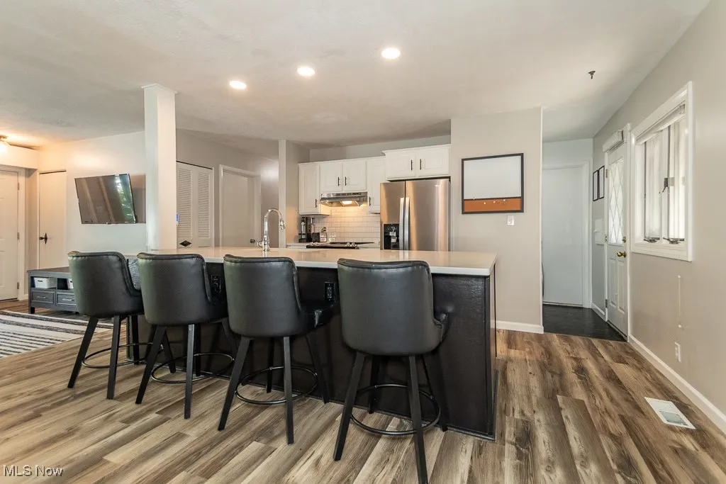 Kitchen with stainless steel refrigerator with ice dispenser, backsplash, dark wood-style floors, recessed lighting, and light countertops