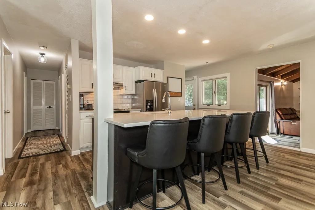 Kitchen with backsplash, dark wood-style flooring, stainless steel refrigerator with ice dispenser, white cabinets, and light countertops