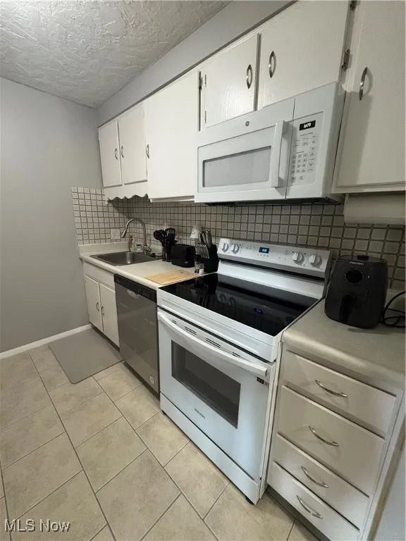 Kitchen with white range oven, backsplash, light tile patterned floors, white cabinetry, and a textured ceiling