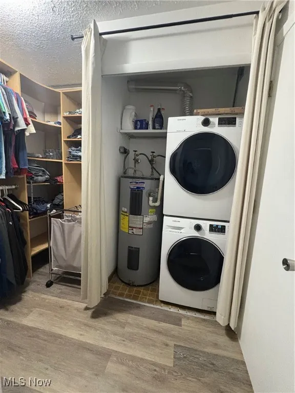 Washroom featuring stacked washer / drying machine, wood finished floors, a textured ceiling, and electric water heater