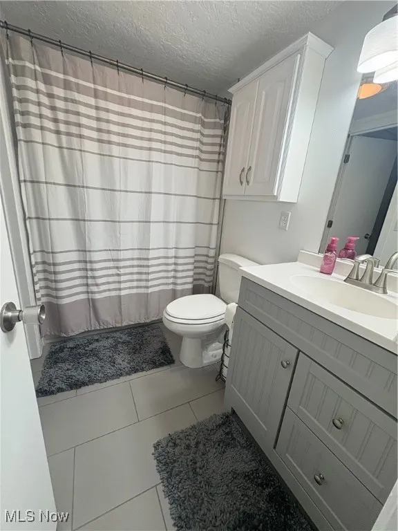 Full bath with tile patterned flooring, vanity, a textured ceiling, and a shower with curtain