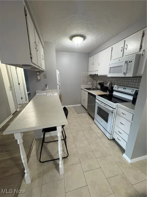 Kitchen with stove, a textured ceiling, backsplash, light tile patterned floors, and white cabinets