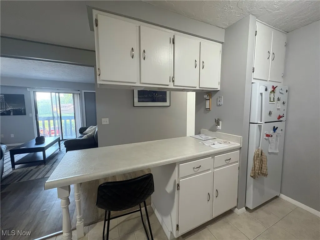 Kitchen featuring a textured ceiling, freestanding refrigerator, white cabinetry, light countertops, and a kitchen bar