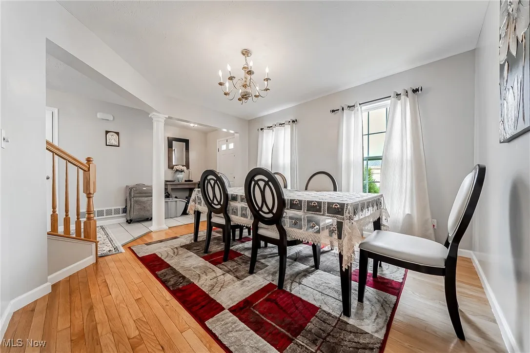 Dining area with light wood-style flooring, a chandelier, ornate columns, and stairway