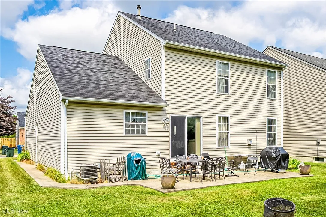 Rear view of house featuring a yard, a shingled roof, a patio, and a fire pit