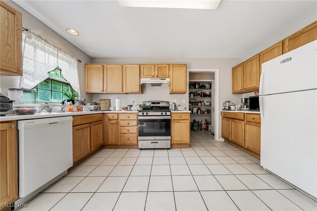 Kitchen with white appliances, light countertops, light tile patterned floors, under cabinet range hood, and recessed lighting