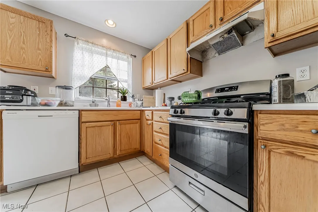 Kitchen featuring gas stove, dishwasher, under cabinet range hood, light tile patterned floors, and light countertops