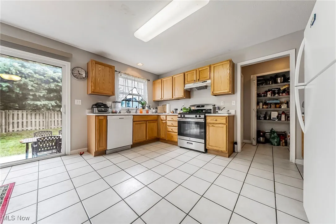 Kitchen featuring white appliances, light tile patterned flooring, light countertops, and under cabinet range hood