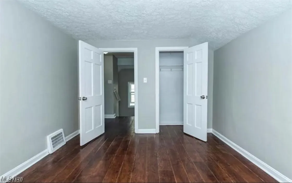 Unfurnished bedroom with a textured ceiling, dark wood-type flooring, and a closet