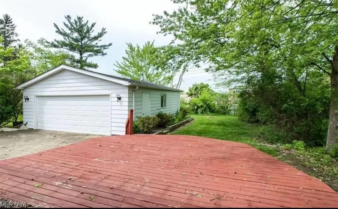 Wooden terrace featuring a detached garage, a lawn, an outdoor structure, and view of wooded area