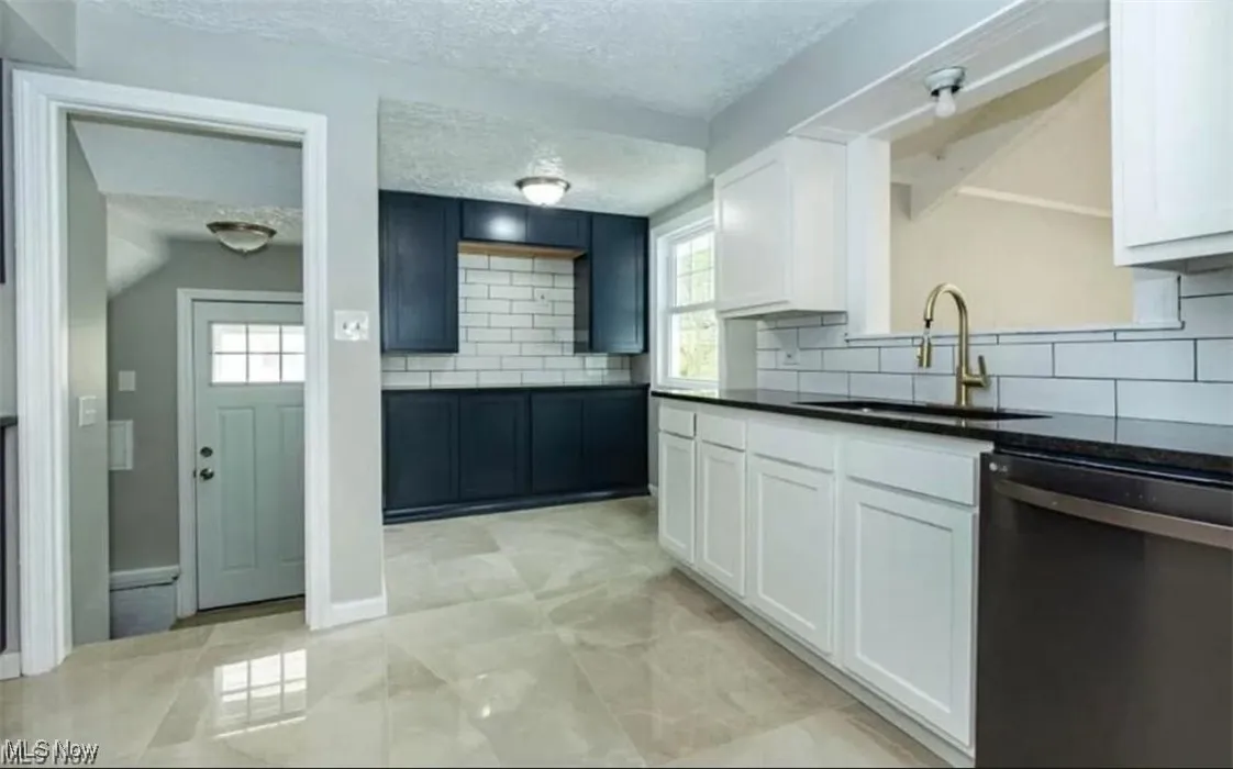Kitchen with a textured ceiling, dishwashing machine, backsplash, white cabinets, and dark countertops