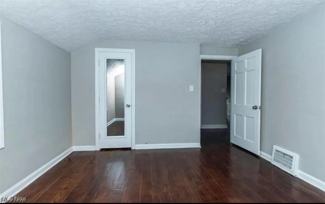 Empty room with a textured ceiling and dark wood finished floors
