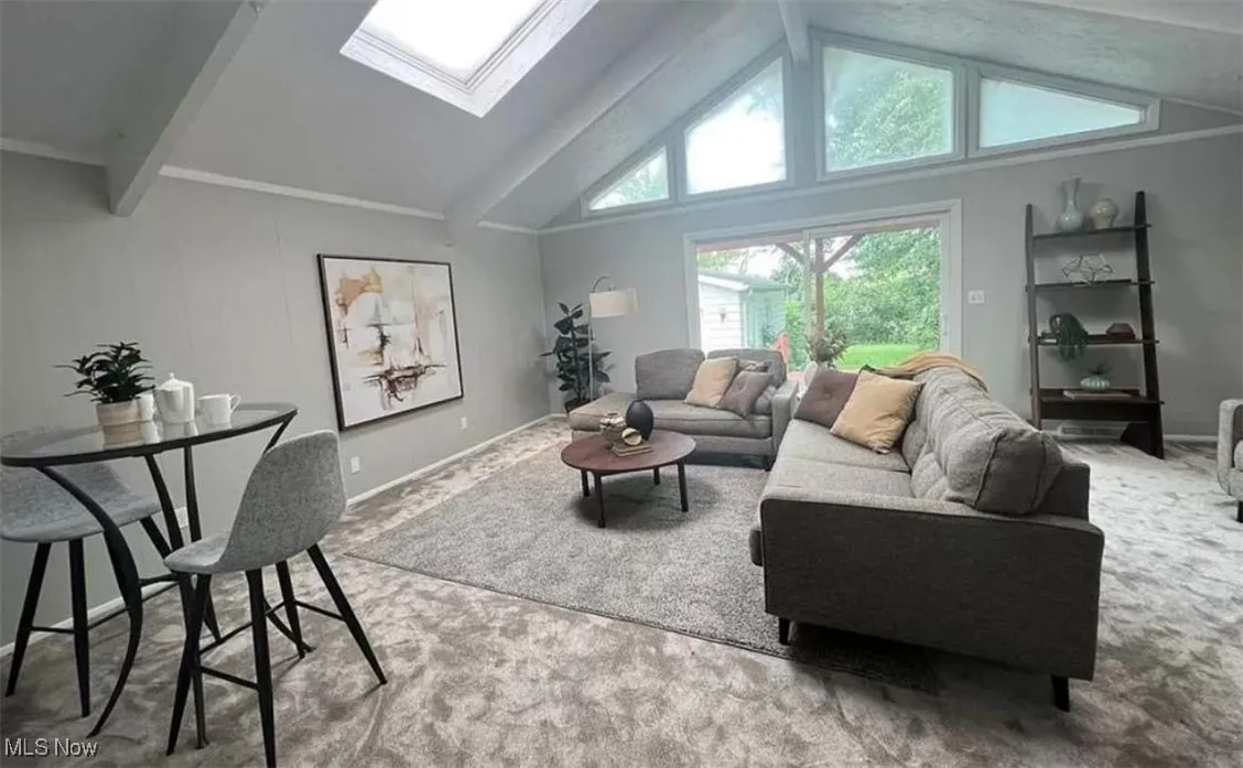 Living room featuring a skylight, beamed ceiling, high vaulted ceiling, and carpet floors