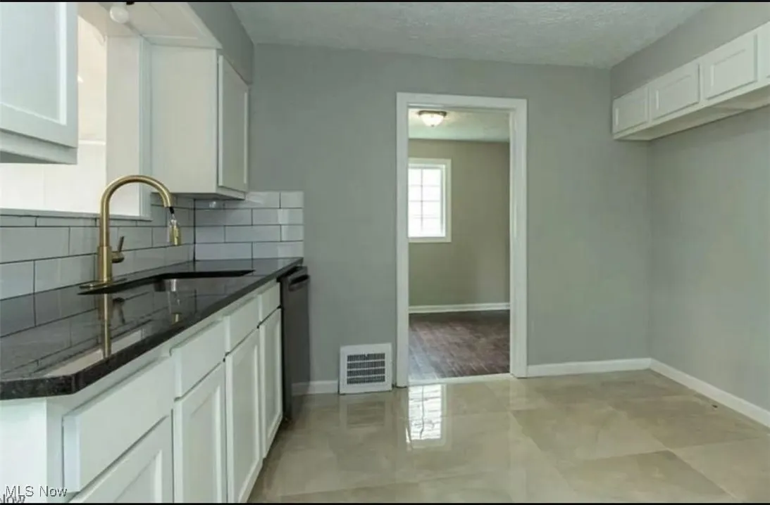 Kitchen with backsplash, white cabinetry, a textured ceiling, dishwasher, and dark stone countertops