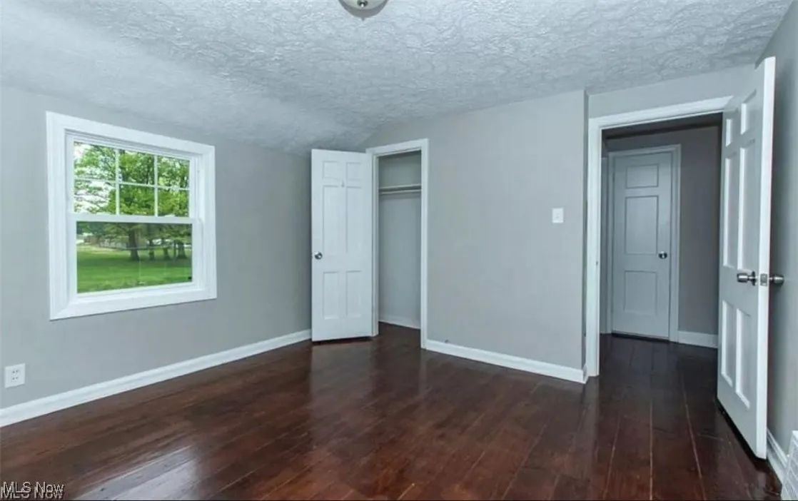 Unfurnished bedroom featuring a textured ceiling, dark wood-type flooring, a closet, and vaulted ceiling