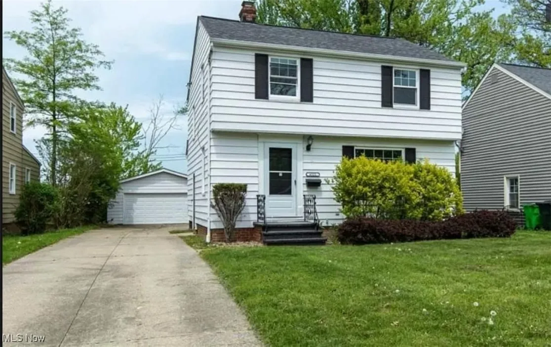 Colonial house with an outbuilding, a chimney, a detached garage, a front lawn, and entry steps