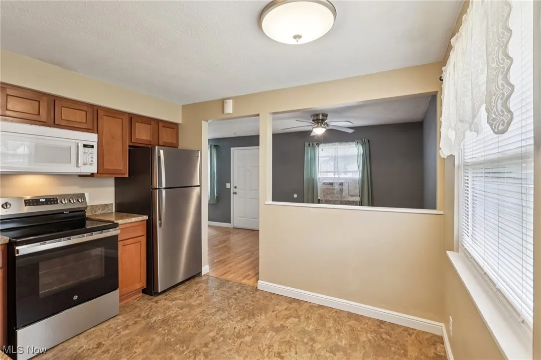 Kitchen with stainless steel appliances, brown cabinets, light countertops, and a ceiling fan