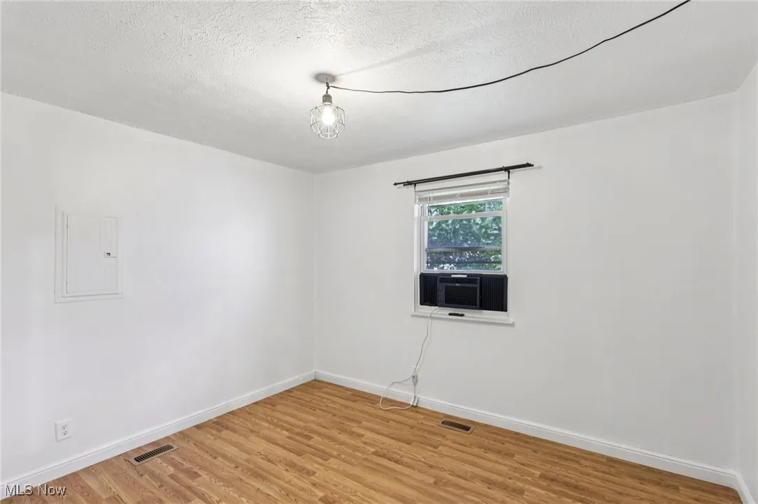 Empty room featuring light wood finished floors, a textured ceiling, and electric panel