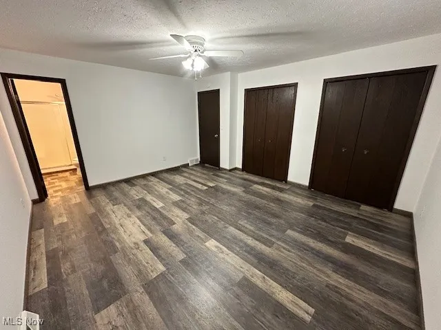 Unfurnished bedroom with dark wood finished floors, a textured ceiling, two closets, and ceiling fan