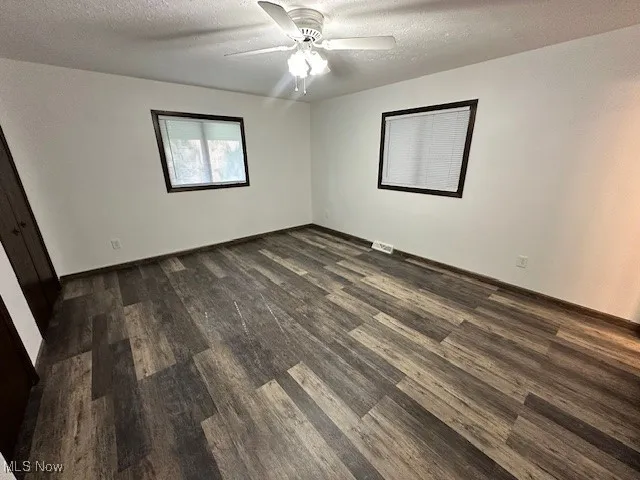 Unfurnished bedroom featuring a textured ceiling, dark wood finished floors, and a ceiling fan