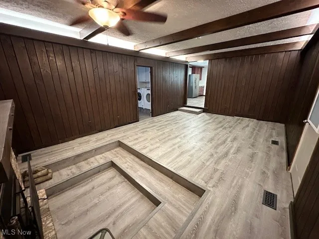 Foyer featuring independent washer and dryer, beam ceiling, a textured ceiling, wood finished floors, and wooden walls