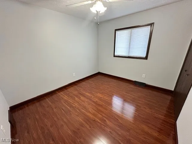 Empty room with a textured ceiling, wood finished floors, and a ceiling fan