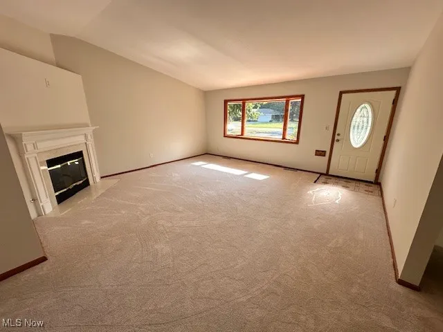 Unfurnished living room featuring light colored carpet, a premium fireplace, and lofted ceiling