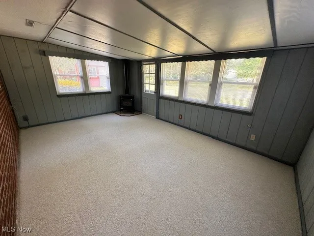 Carpeted spare room with wood walls, a wood stove, and lofted ceiling