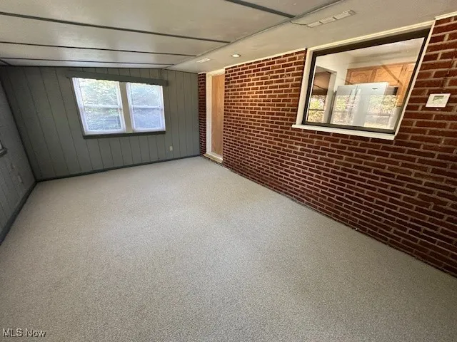 Unfurnished room featuring brick wall and light carpet