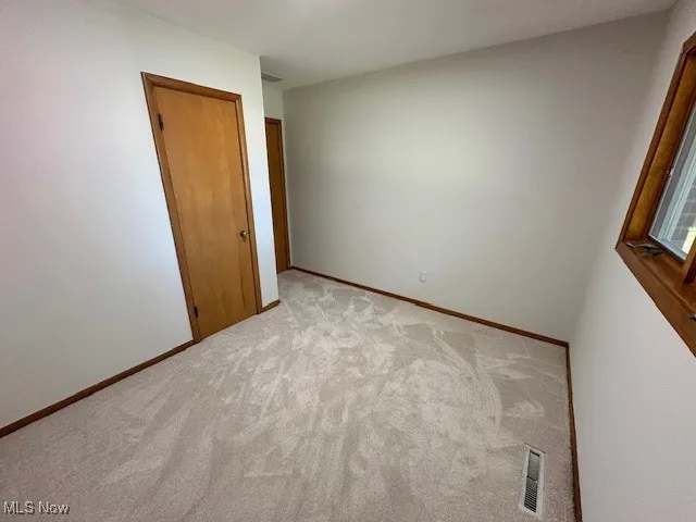 Unfurnished bedroom with light carpet and baseboards