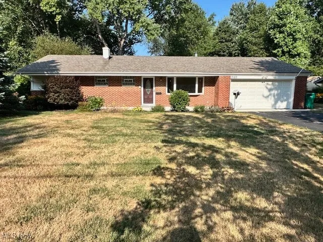 Ranch-style house featuring an attached garage, asphalt driveway, brick siding, and a front yard