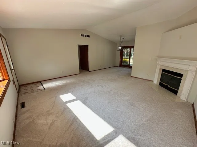 Unfurnished living room with light colored carpet, lofted ceiling, and a fireplace
