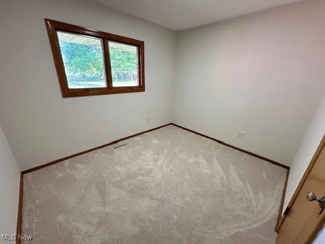 Unfurnished room featuring light carpet and baseboards