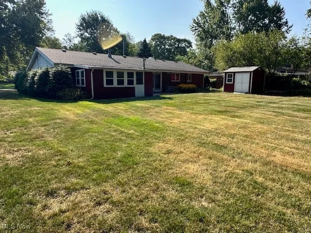 Back of house with a storage unit and a yard