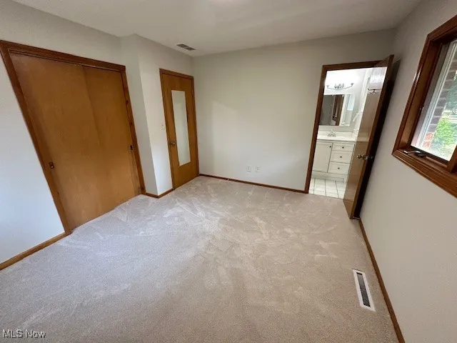 Unfurnished bedroom featuring light colored carpet, a closet, and ensuite bathroom