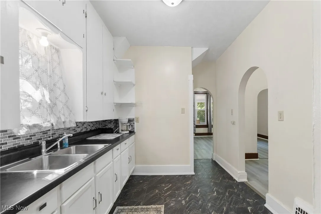 Kitchen with arched walkways, white cabinets, dark countertops, open shelves, and backsplash
