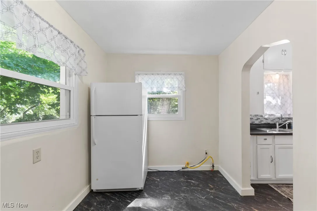 Kitchen with freestanding refrigerator, dark marble finish flooring, white cabinets, arched walkways, and decorative backsplash