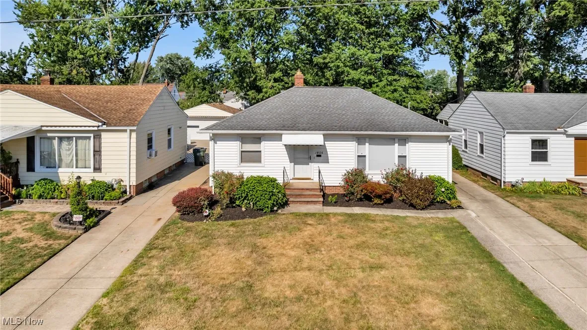 Bungalow-style home featuring roof with shingles, a front lawn, concrete driveway, and a chimney