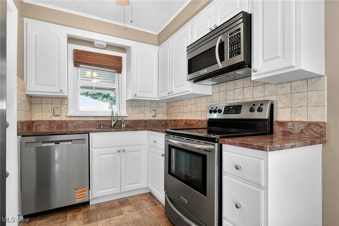 Kitchen featuring appliances with stainless steel finishes, backsplash, white cabinetry, and stone finish floors