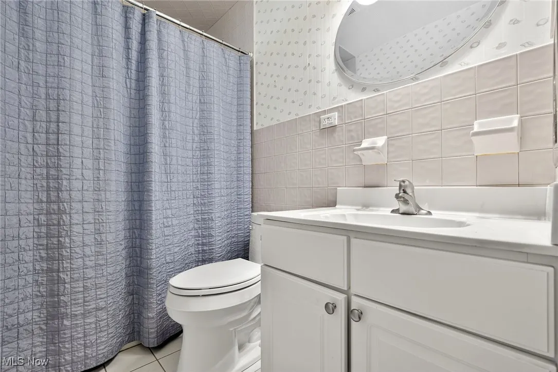 Full bathroom featuring tile walls, vanity, wallpapered walls, tile patterned floors, and a wainscoted wall