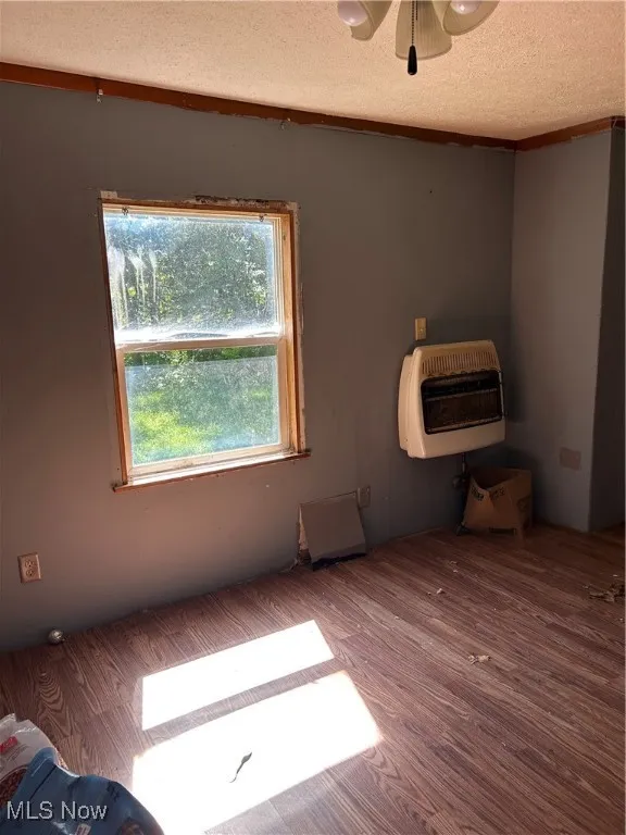 Unfurnished room featuring heating unit, wood finished floors, a textured ceiling, and a ceiling fan