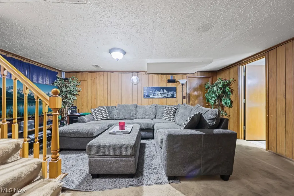 Living area with wooden walls, carpet floors, stairs, and a textured ceiling