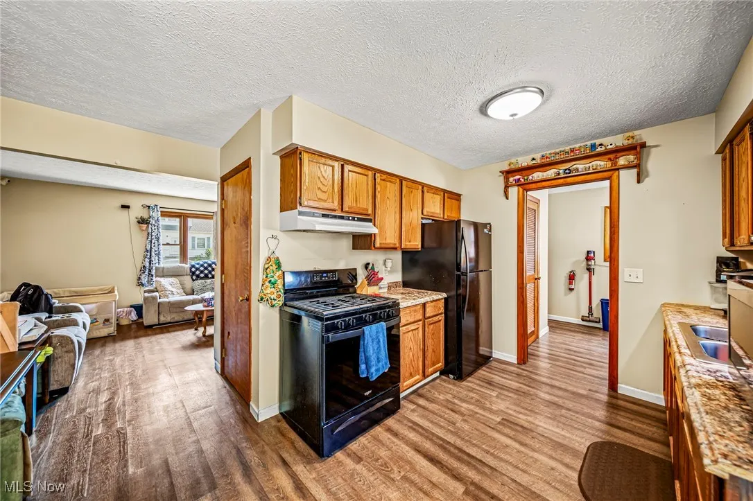 Kitchen featuring black appliances, a textured ceiling, wood finished floors, open floor plan, and brown cabinetry