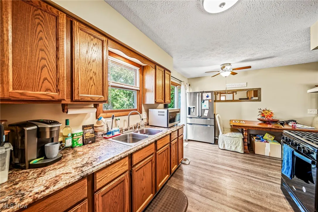 Kitchen featuring appliances with stainless steel finishes, brown cabinets, light wood finished floors, a textured ceiling, and ceiling fan
