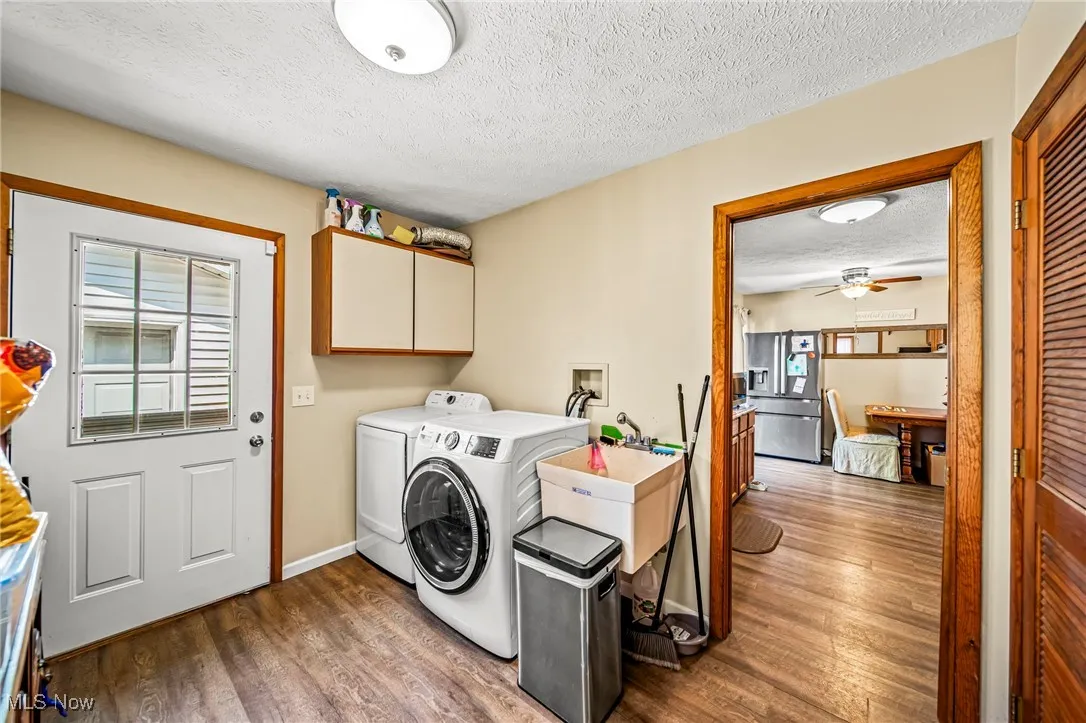 Washroom featuring cabinet space, a textured ceiling, washing machine and clothes dryer, wood finished floors, and ceiling fan