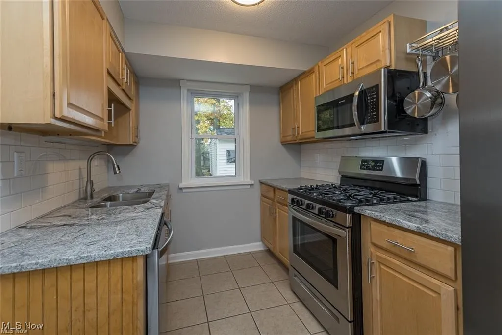 Kitchen featuring backsplash, stainless steel appliances, light tile patterned flooring, light stone counters, and a textured ceiling