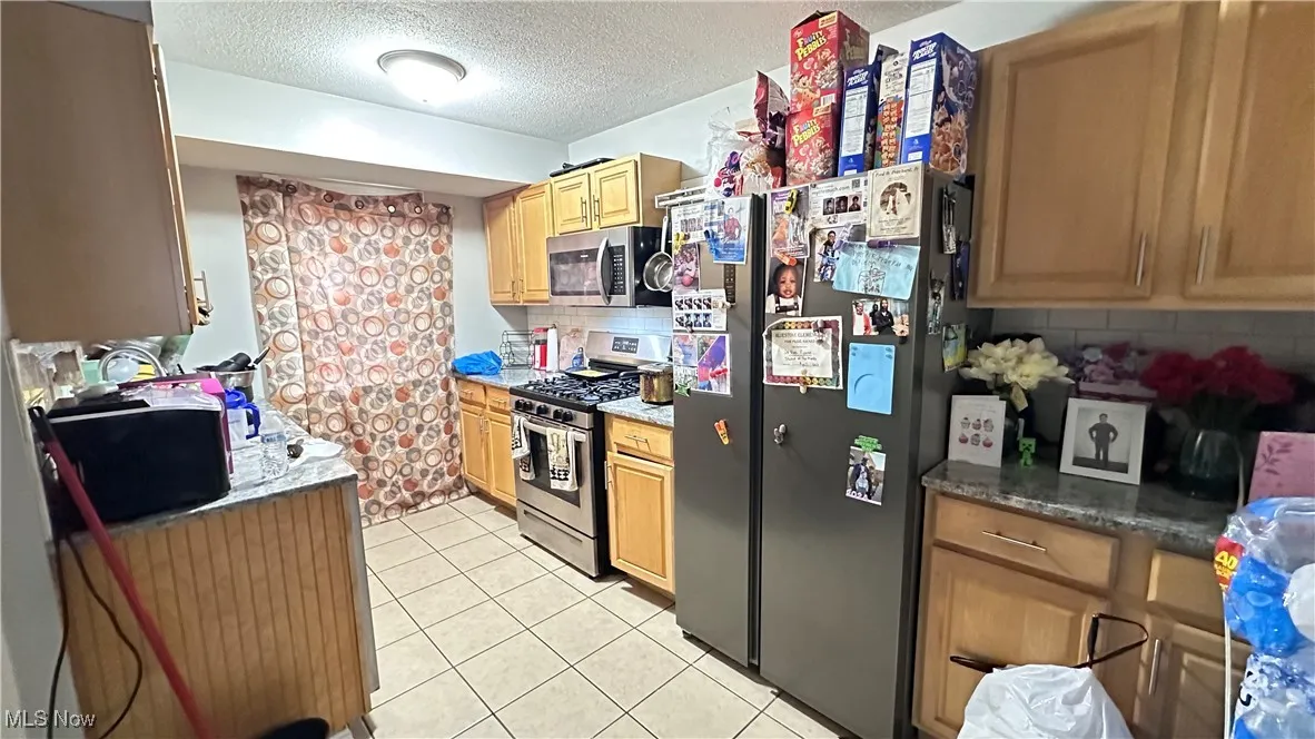 Kitchen with appliances with stainless steel finishes, a textured ceiling, light tile patterned floors, and backsplash