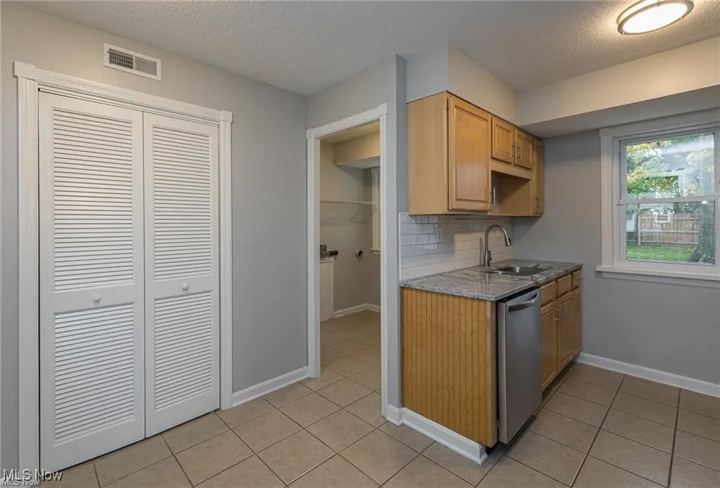 Kitchen with a textured ceiling, tasteful backsplash, light tile patterned flooring, stainless steel dishwasher, and light stone countertops