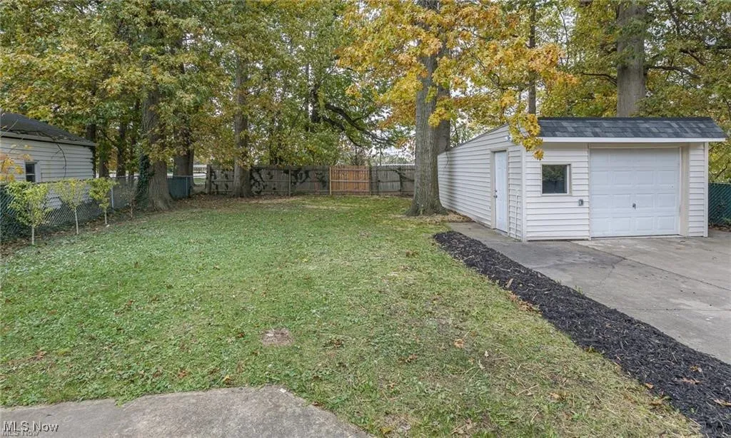 Fenced backyard featuring an outbuilding, concrete driveway, a detached garage, and view of wooded area